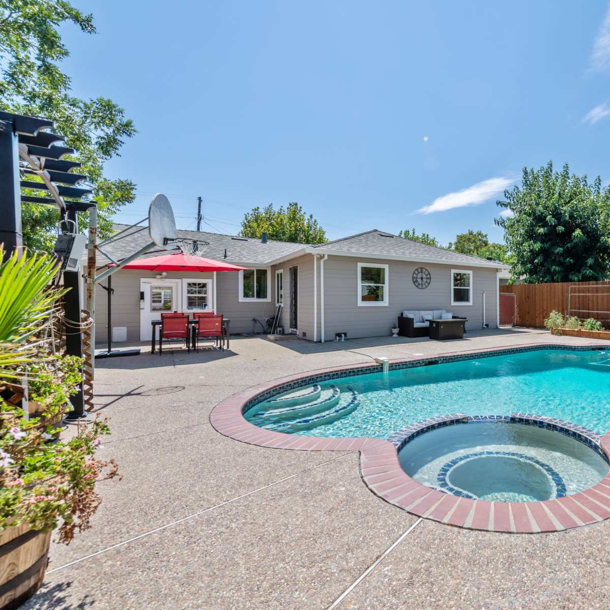 A backyard pool area featuring a kidney-shaped pool with a spa, surrounded by a patio and landscaped plants.