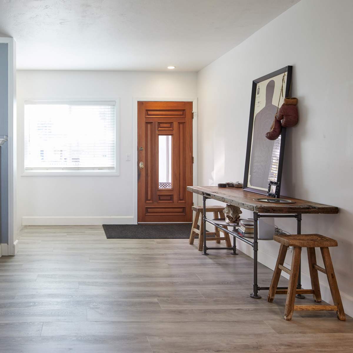 A minimalist living room featuring a white brick fireplace, a wooden entry door, and a simple wooden table with stools.
