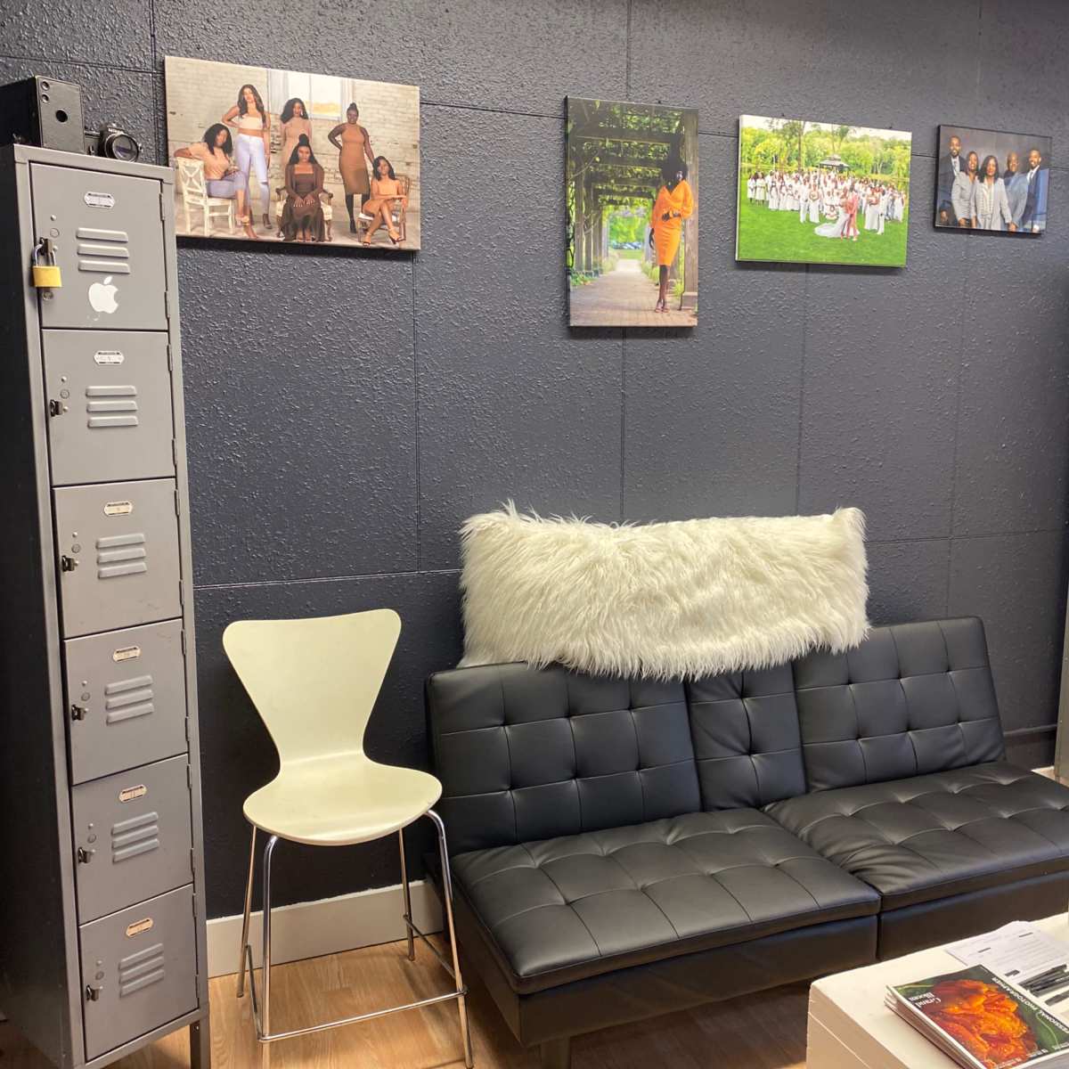 A modern sitting area with a black couch, a white chair, gray lockers, and framed photographs on a dark wall.