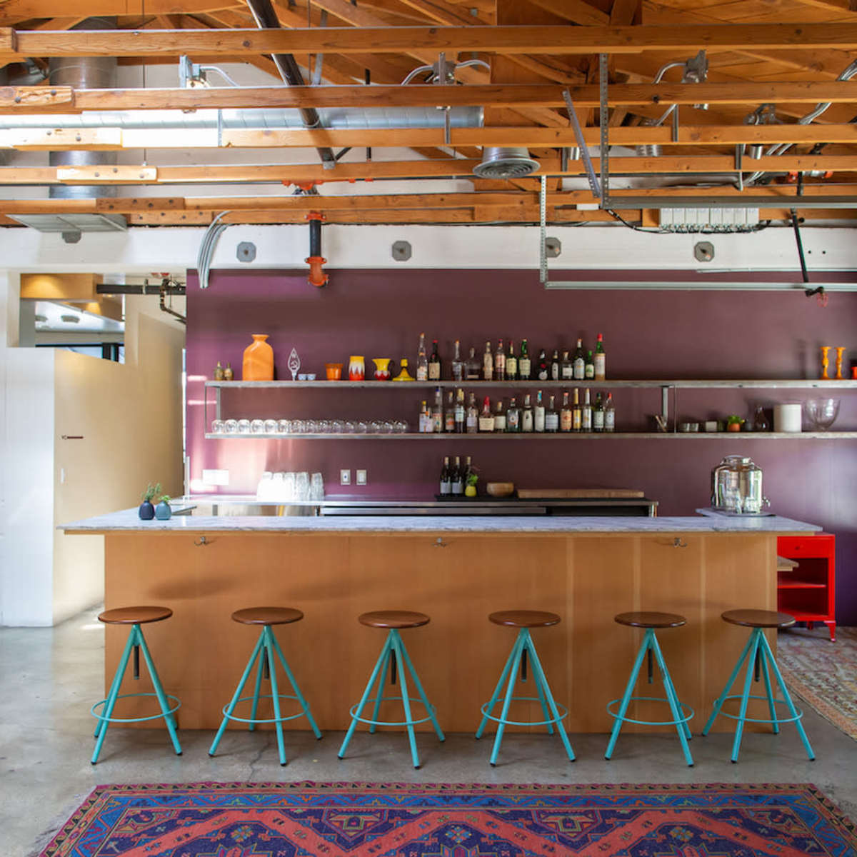 A modern kitchen with a central island bar featuring stools, open shelving displaying various bottles, and a mix of rustic and contemporary design elements.