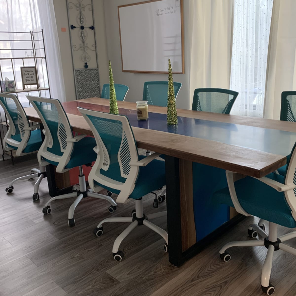 A modern conference room features a long wooden table with a glass center and several teal office chairs arranged around it.