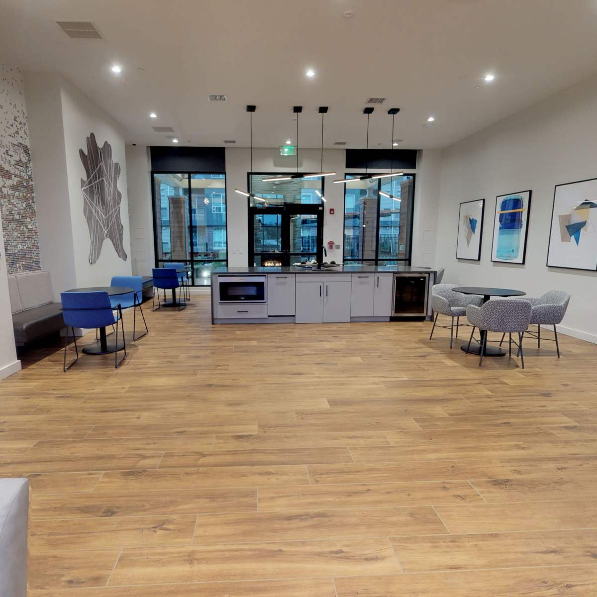 A modern lounge area featuring a kitchen counter, seating arrangements, and large windows.