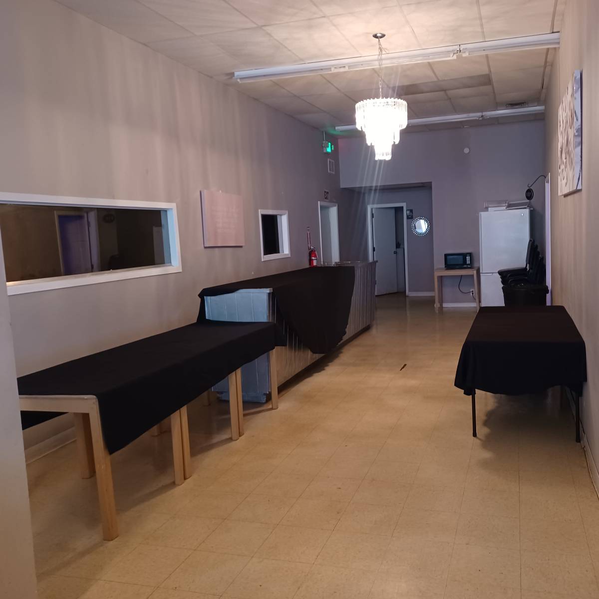 A hallway with several tables covered in black cloth and a chandelier hanging from the ceiling.