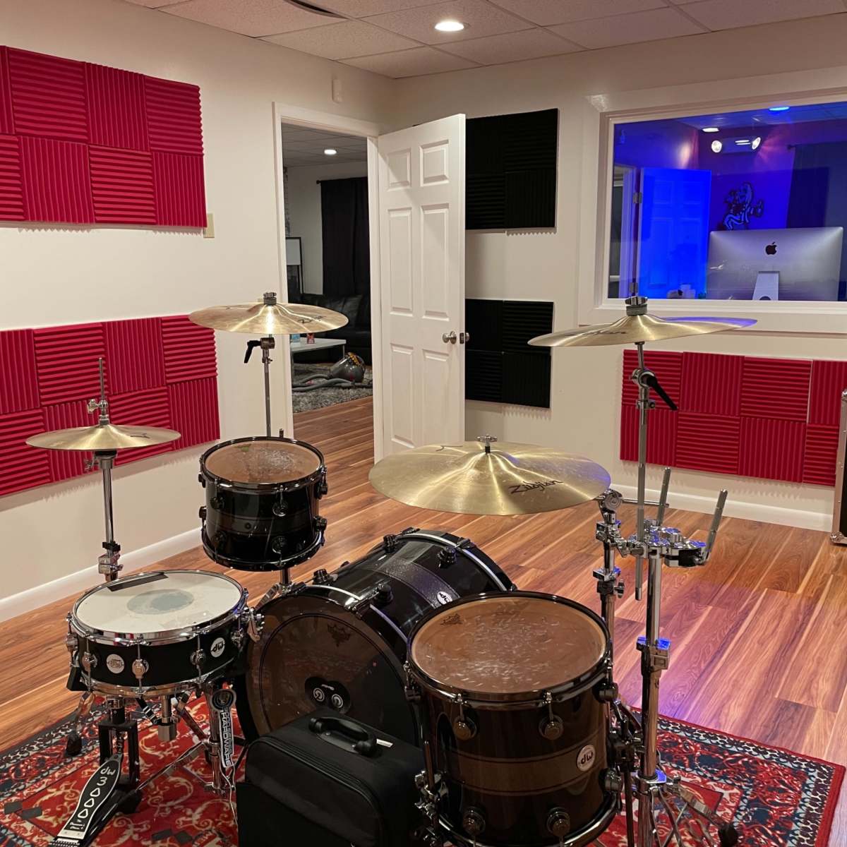A drum set is positioned in a soundproofed room with red and black acoustic panels on the walls.