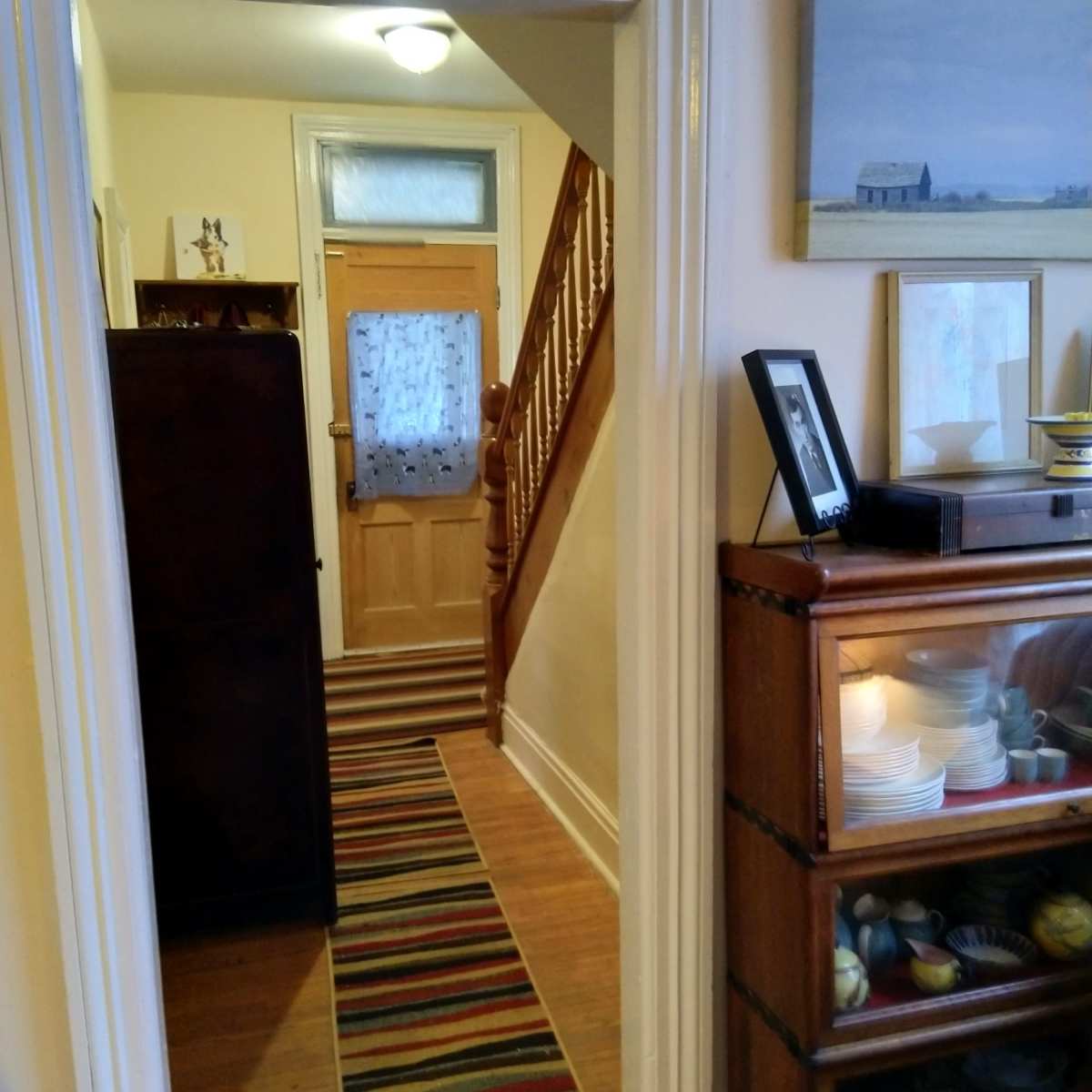 A narrow hallway leads to a wooden door at the far end, with a staircase on the left and a display cabinet on the right.