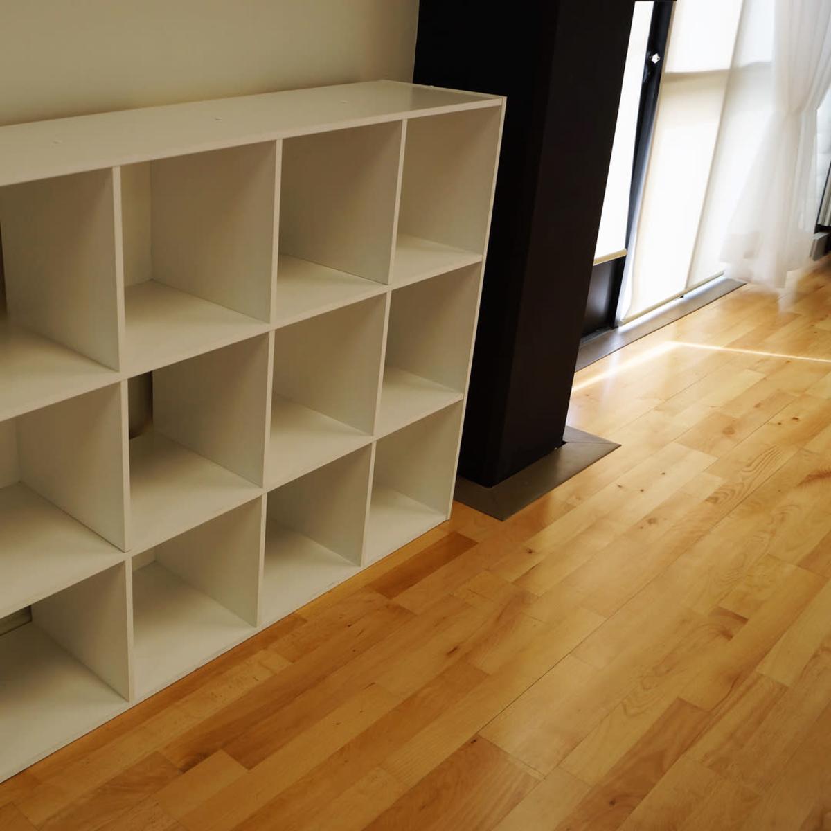 A white shelving unit with twelve square compartments positioned against a wall on a hardwood floor.