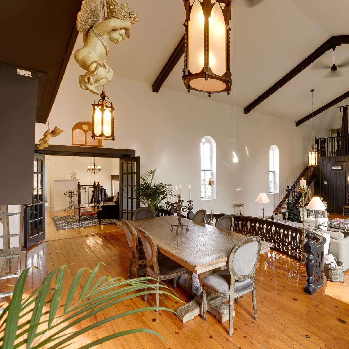 A large, open-plan living area with a dining table, decorative lighting fixtures, and a staircase leading to a lofted space.