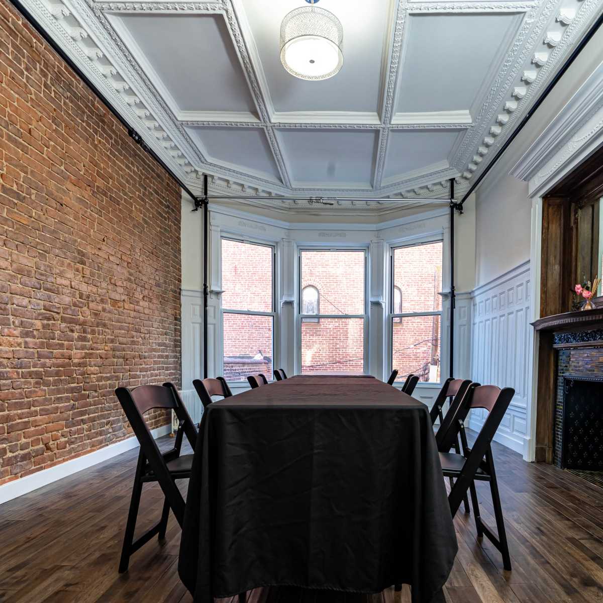 A conference room features a long table with chairs, brick and white-paneled walls, and large windows allowing natural light.