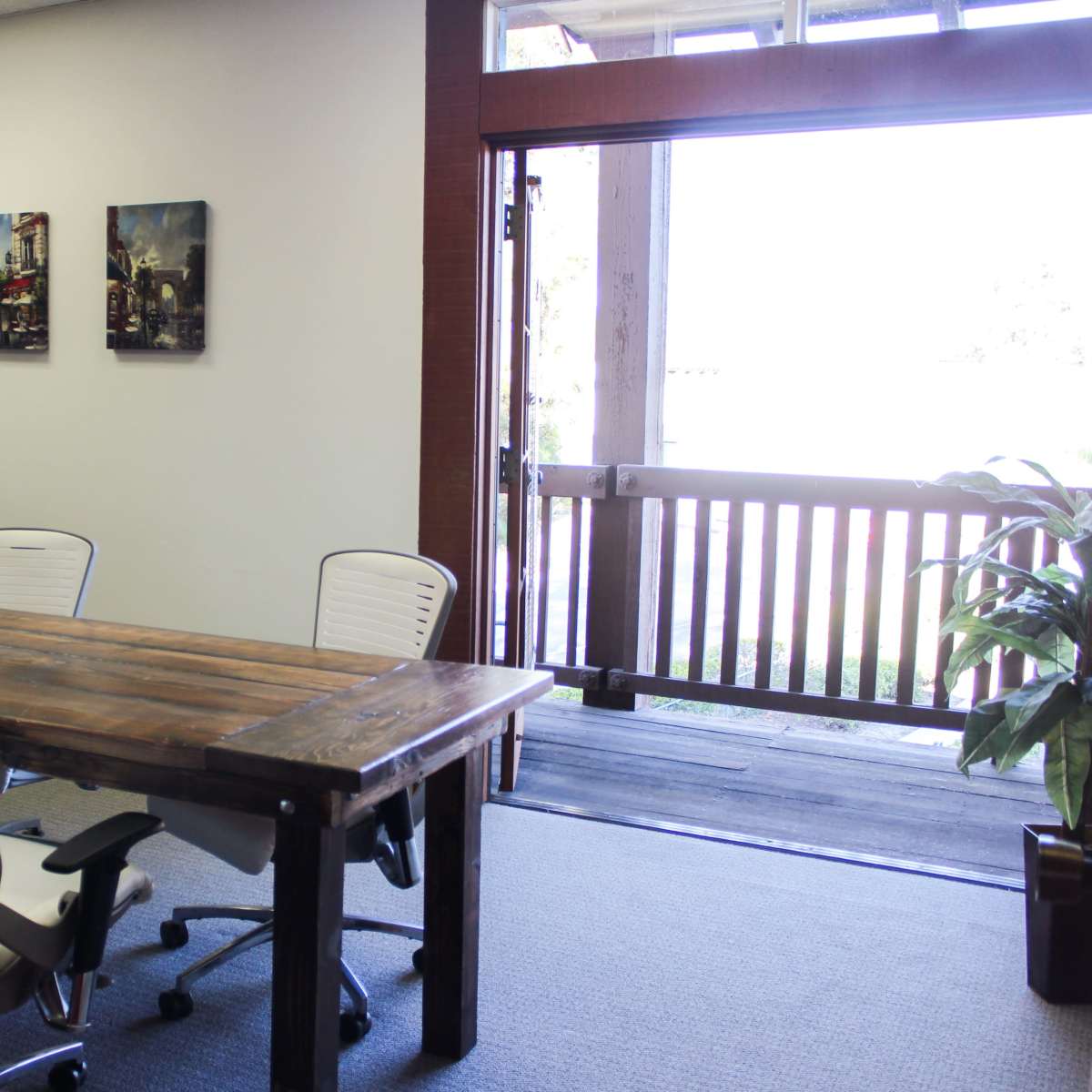 A conference room features a wooden table surrounded by white chairs, with a door leading to an outdoor area visible in the background.