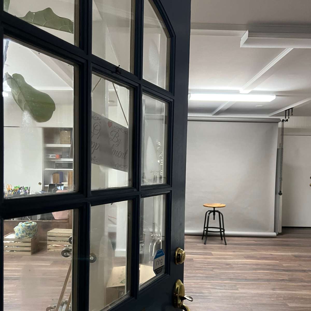 A partially open blue door leading into a sparsely furnished studio with a stool and a plain backdrop.