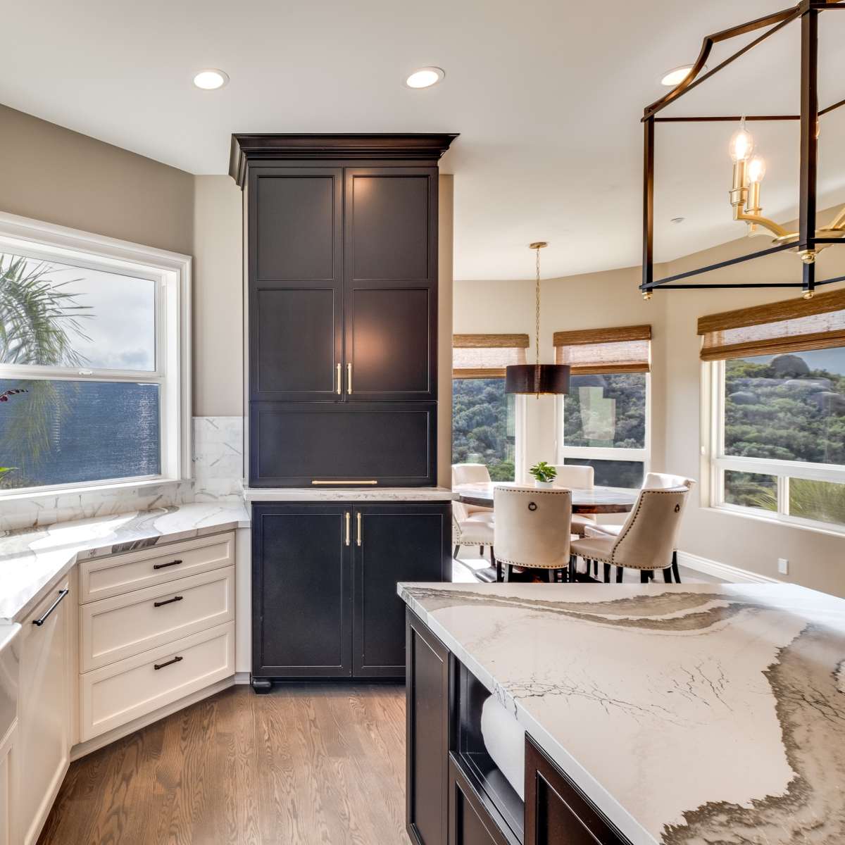 A modern kitchen featuring dark cabinetry, a white marble countertop, and a large window with a view of greenery.
