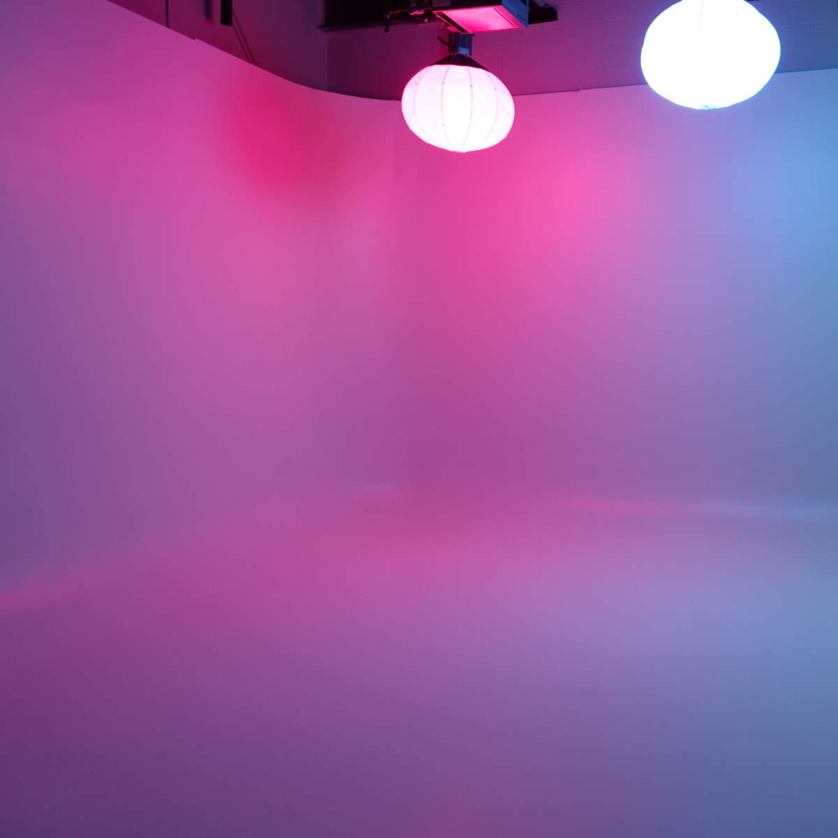 A spacious studio backdrop illuminated with colored lights and three hanging lanterns.