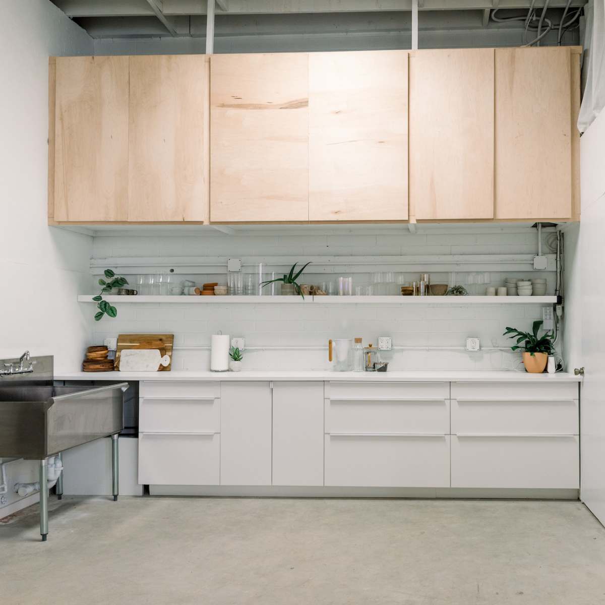A modern kitchen with white cabinetry, wooden overhead cabinets, and minimal decor along the countertop.