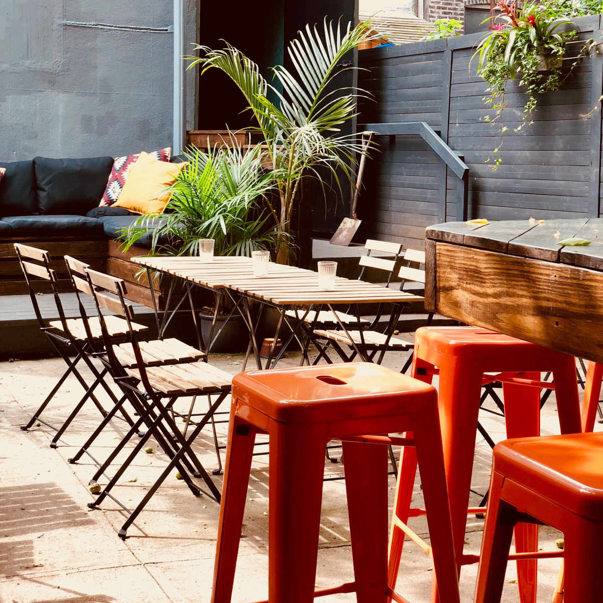 A small outdoor seating area with metal chairs and tables surrounded by greenery and string lights overhead.