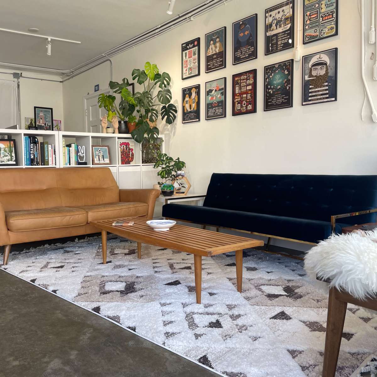 A stylish living room with a brown leather sofa, a blue velvet couch, a wooden coffee table, and a rug, all arranged around a wall featuring framed artwork.