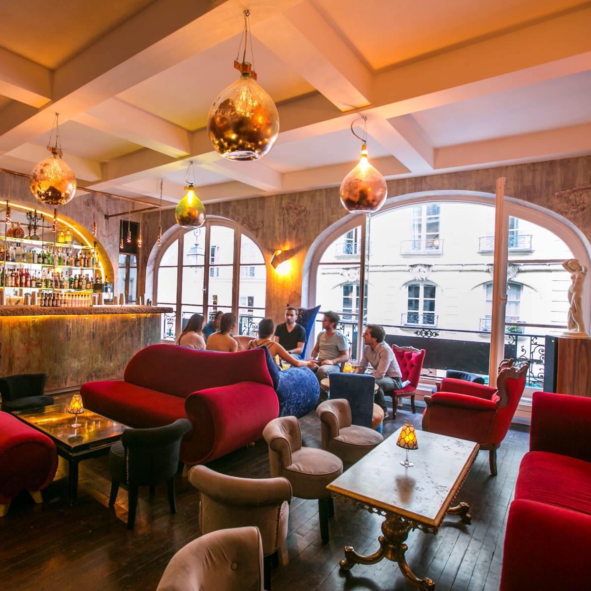 A stylish bar interior with a curved bar, plush red couches, and decorative pendant lighting.