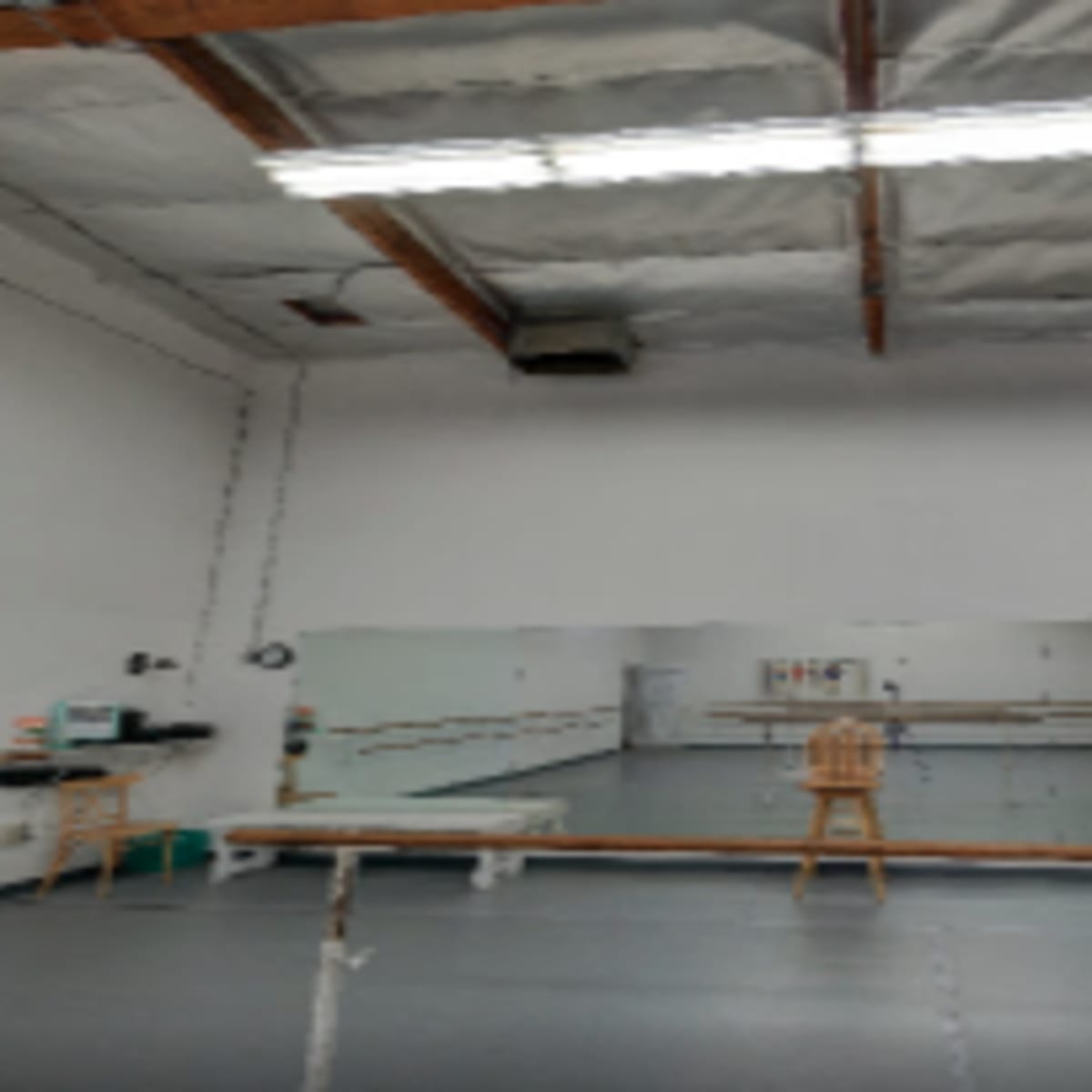 An empty dance studio with mirrors, a wooden barre along the wall, and overhead lighting.