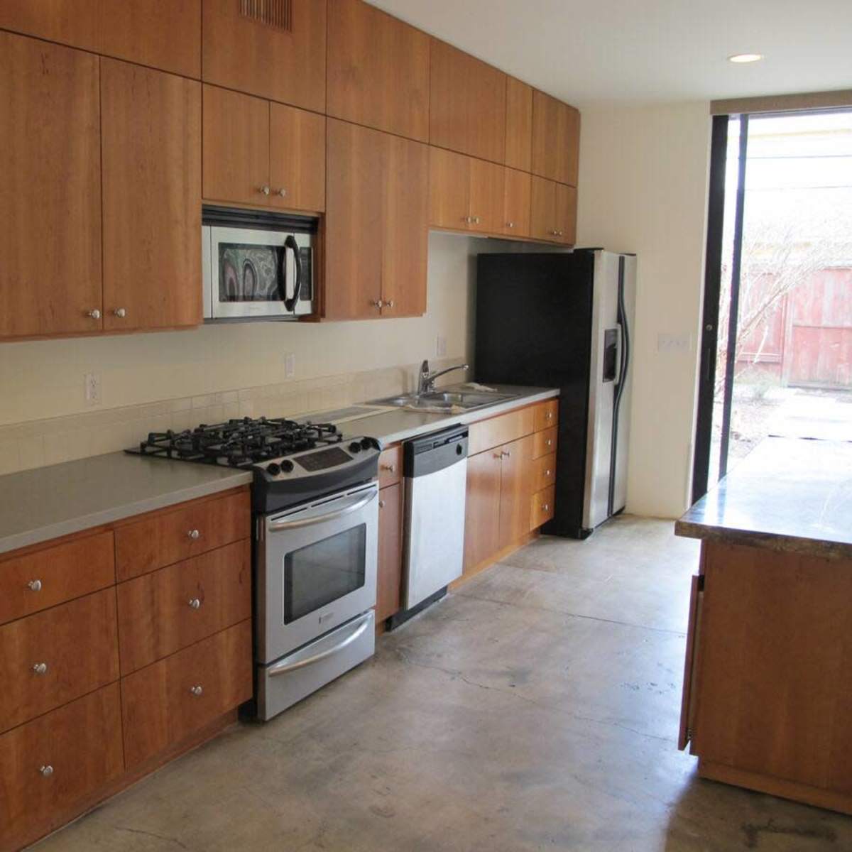 A modern kitchen features wooden cabinetry, stainless steel appliances, and a concrete countertop.