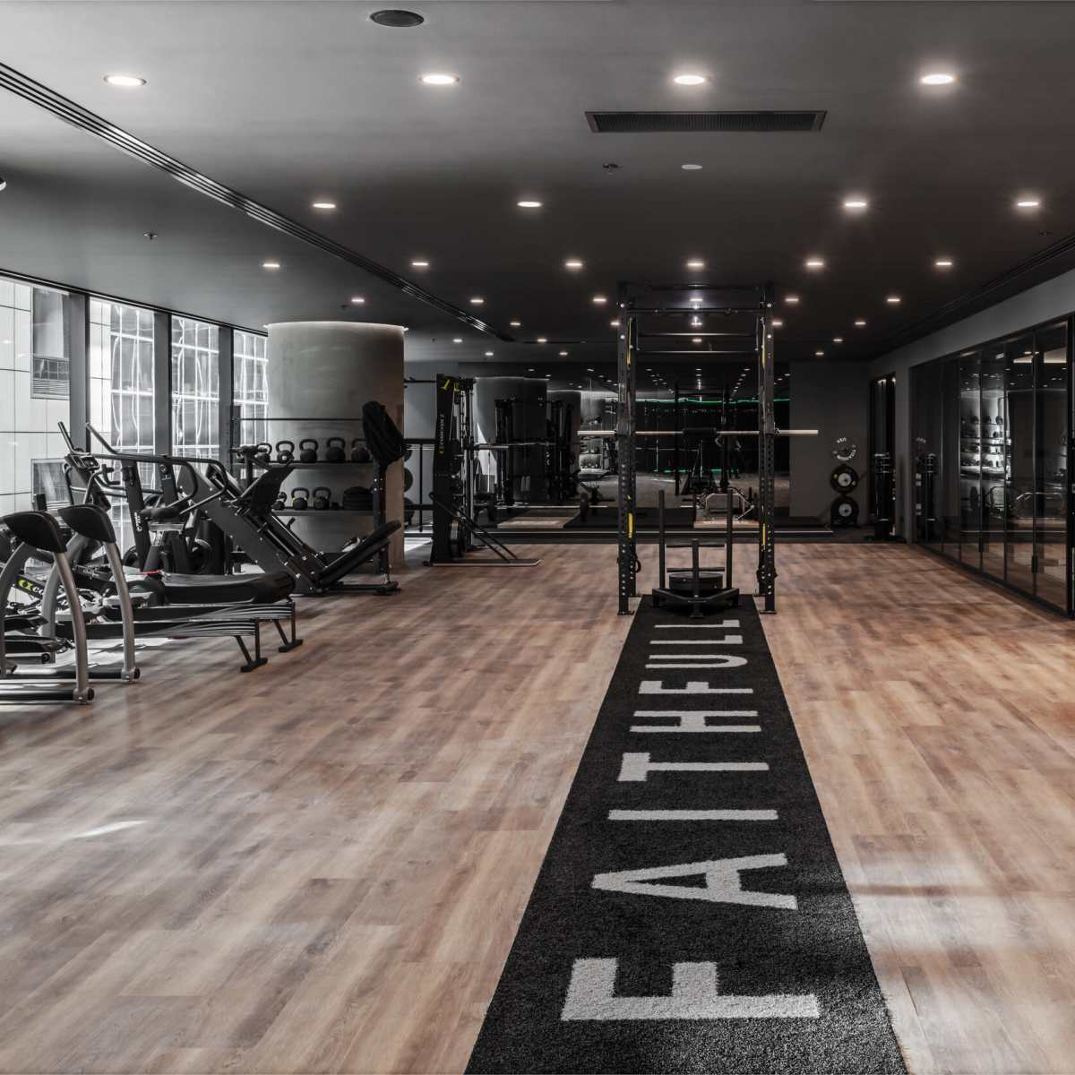 A modern gym features wooden flooring, workout equipment on one side, and a wall adorned with greenery and a fitness area.
