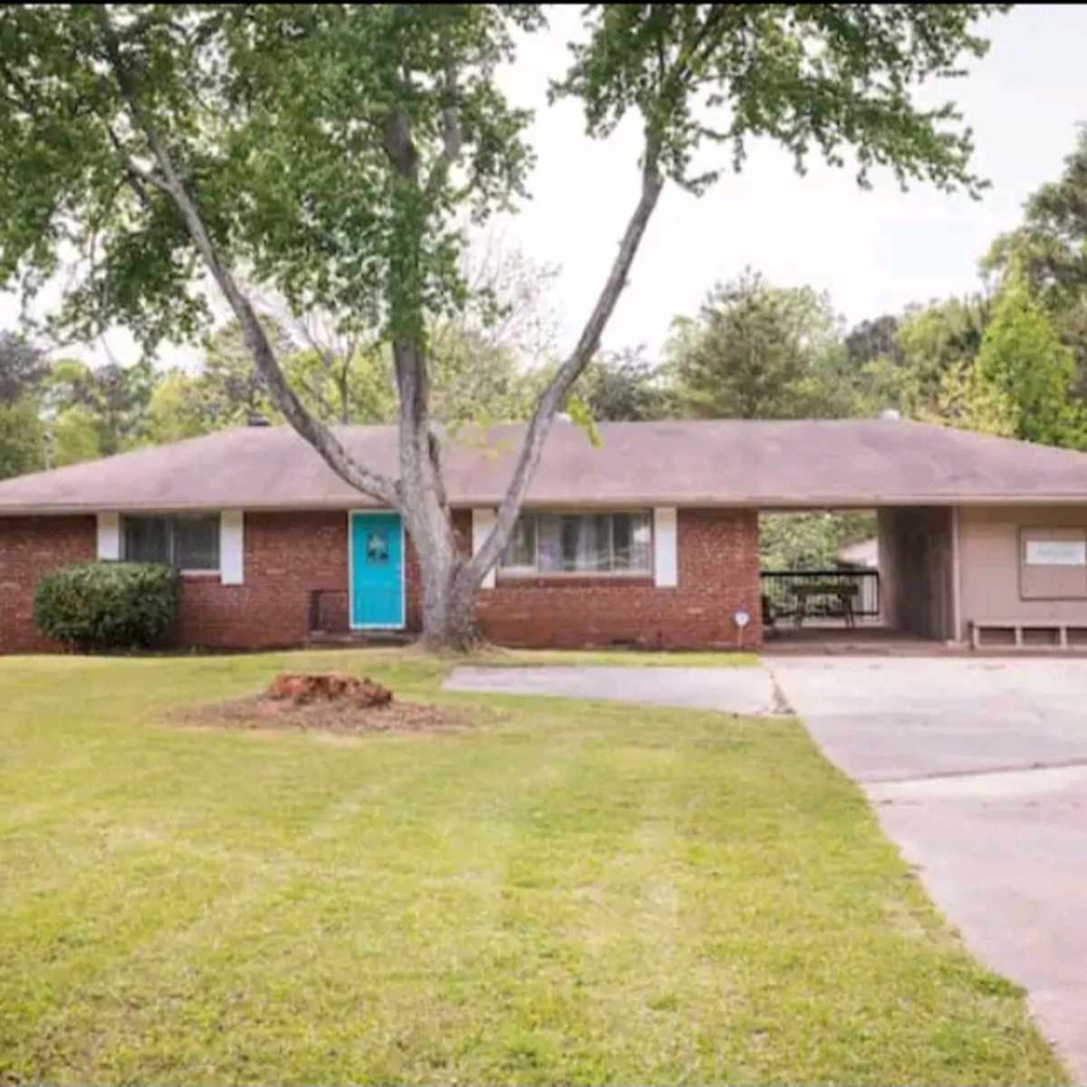 A single-story brick house with a teal front door, surrounded by a green lawn and a driveway.