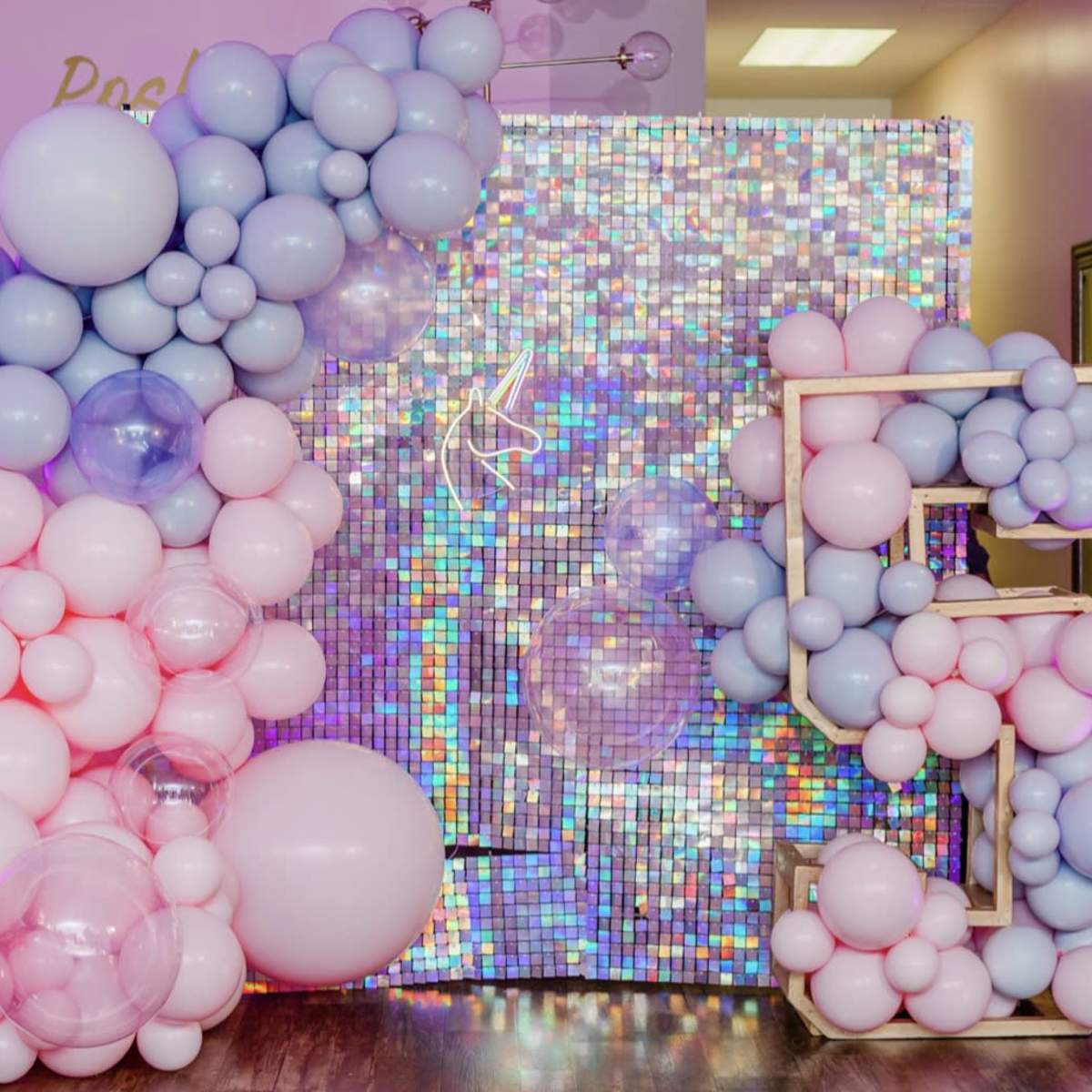 A decorative wall composed of variously sized pink and blue balloons is set against a shimmering, multicolored backdrop.
