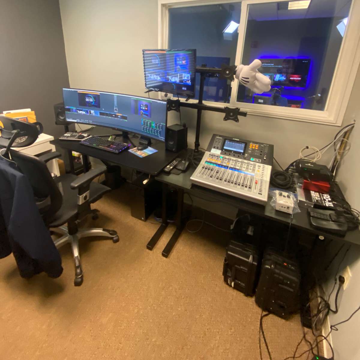 A multimedia production workspace featuring dual computer monitors, audio equipment, and a desk with various devices.