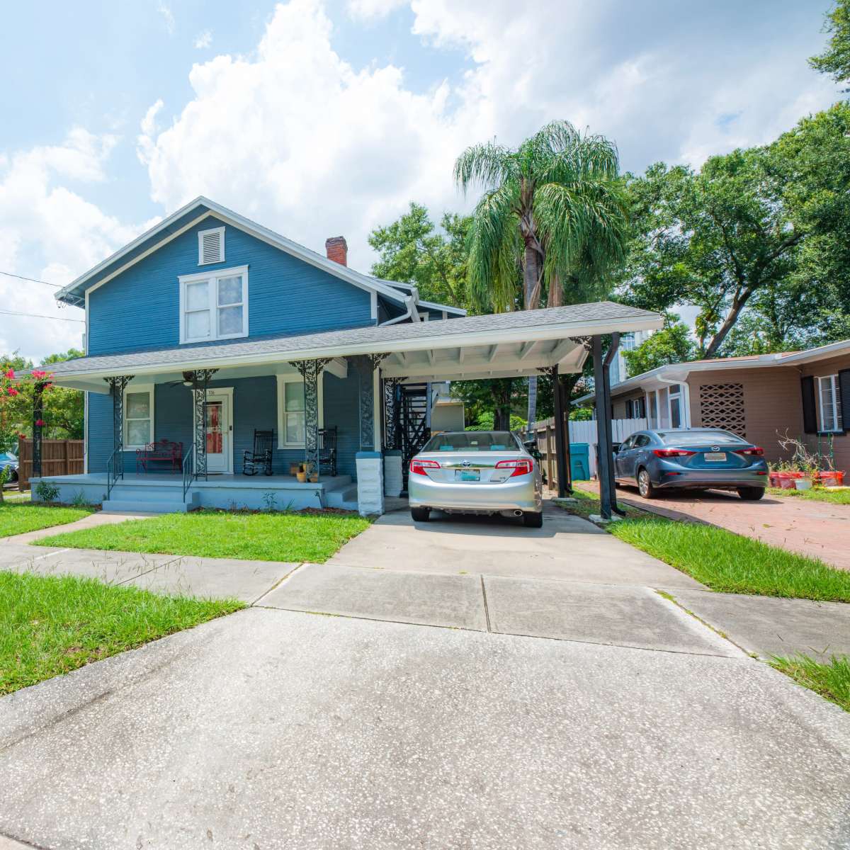 A blue two-story house with a covered porch and two parked cars sits on a well-maintained lawn.