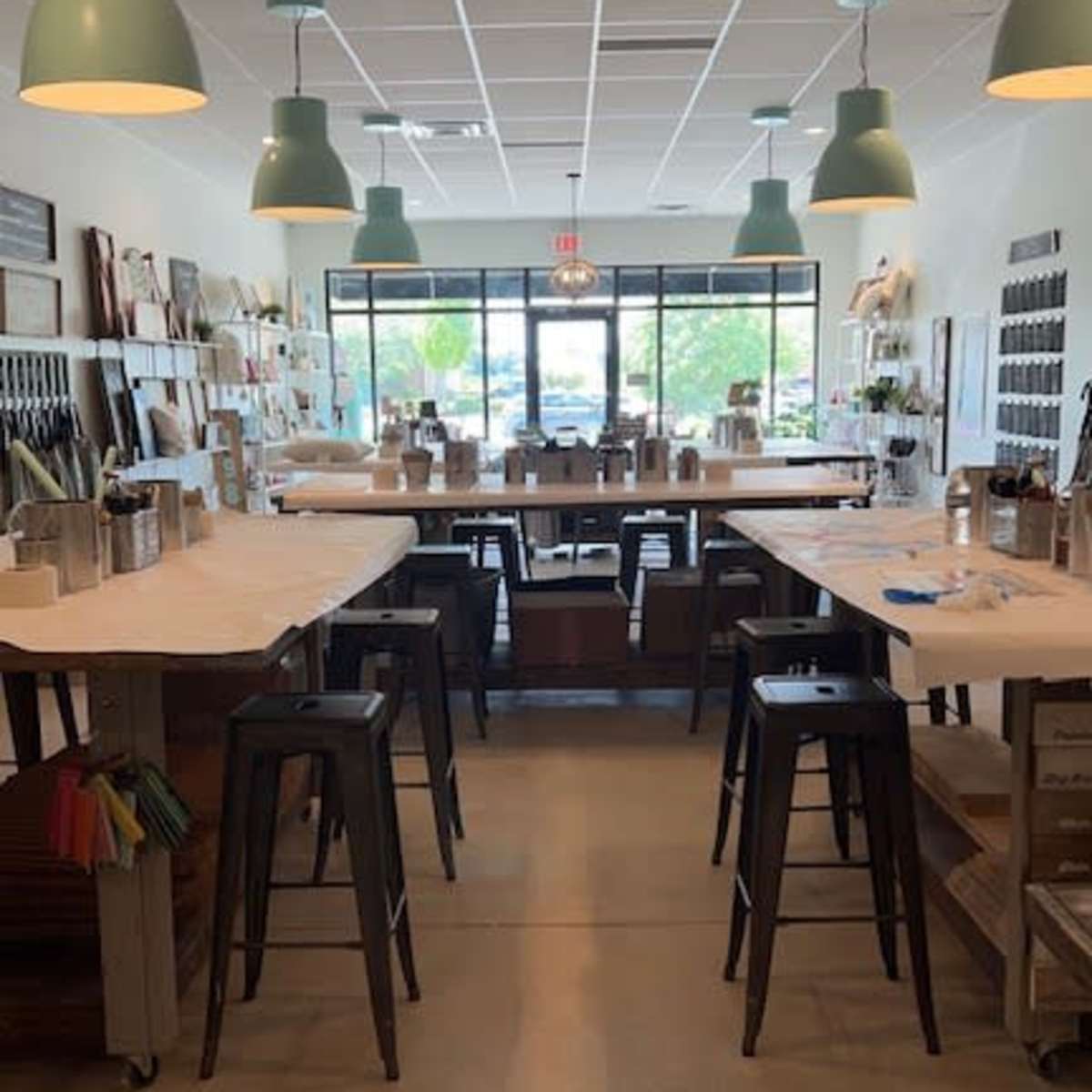 An art studio with several wooden tables, metal stools, and large windows allowing natural light to enter.