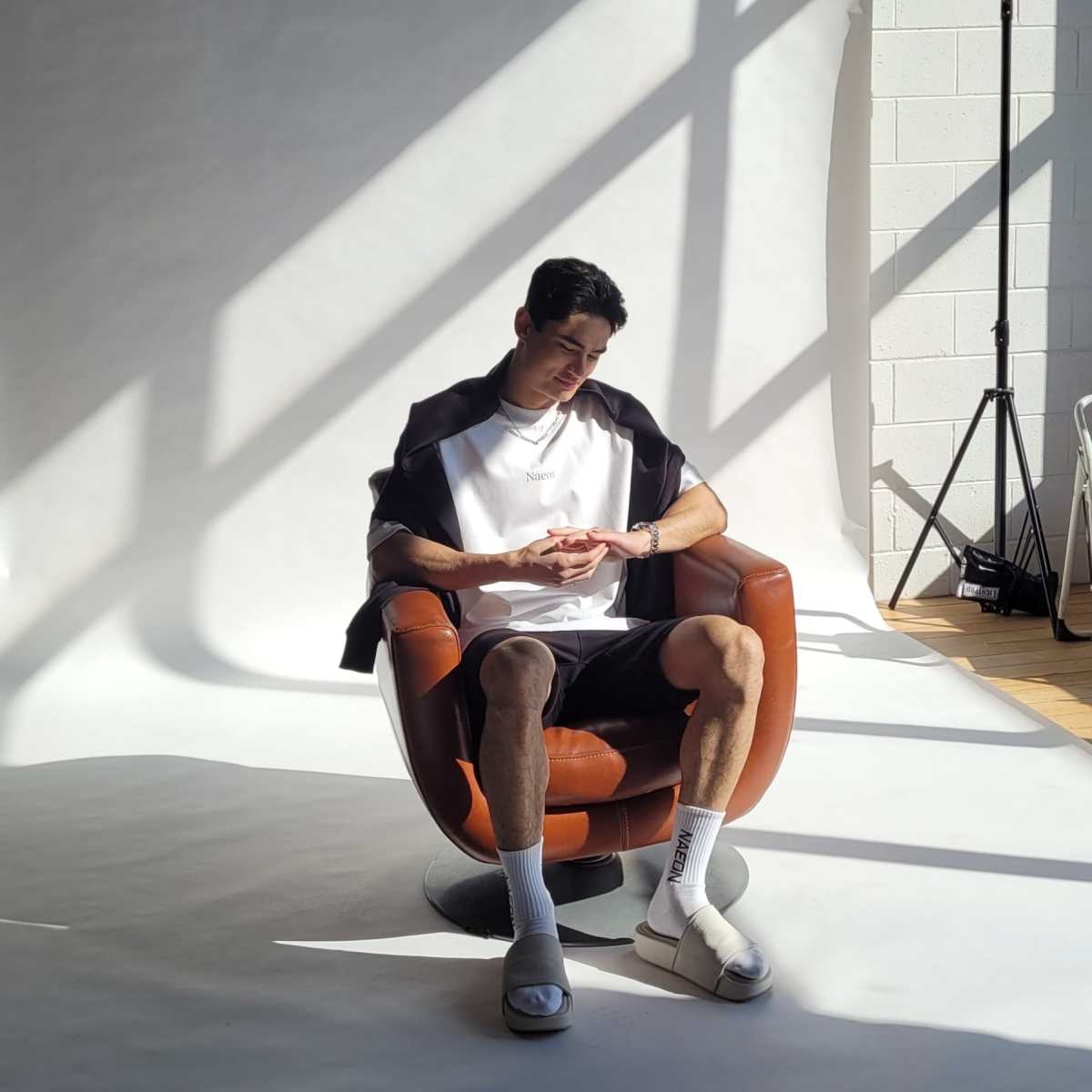 A person sits in a brown chair, reading a book in a well-lit studio with shadows cast by overhead beams.