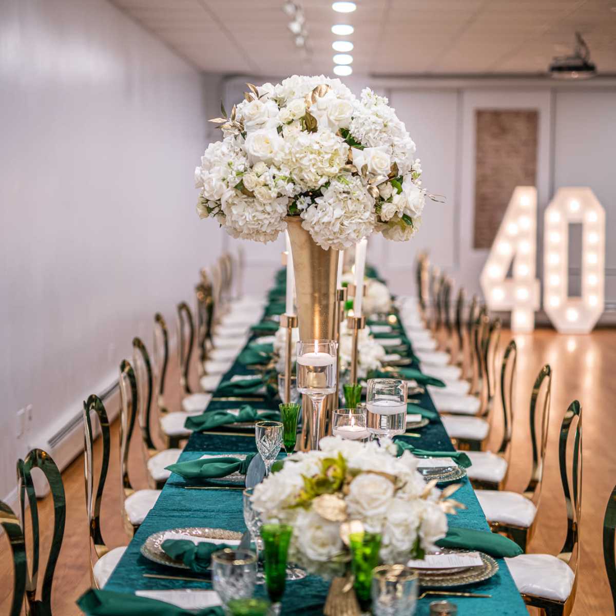 A long banquet table is set with green tablecloths, white floral centerpieces, and decorative candles, with large illuminated numbers "40" in the background.