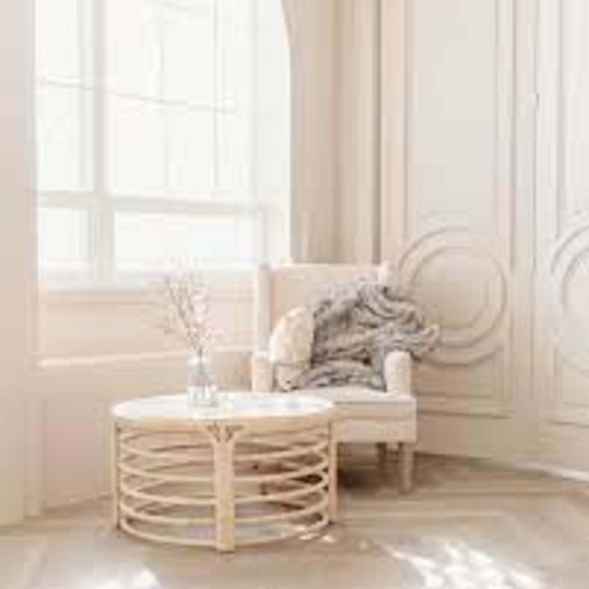 A cozy armchair is positioned beside a round coffee table in a sunlit room with tall windows and decorative doors.