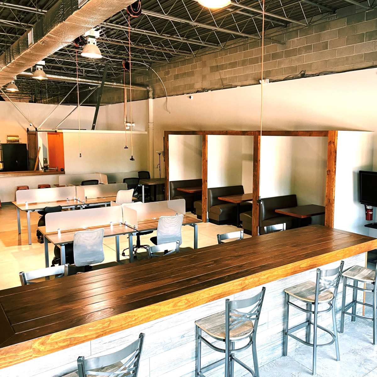 A contemporary interior of a casual dining space featuring a long wooden bar, several tables, and seating booths along one wall.