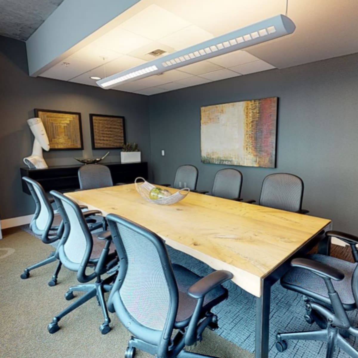 A modern conference room with a large wooden table surrounded by ergonomic chairs and minimalist decor.