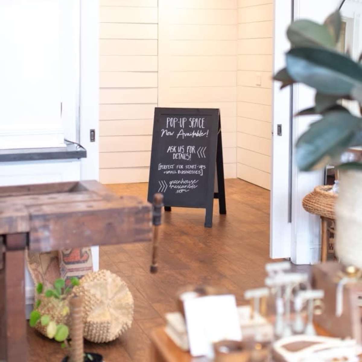 A pop-up space sign stands on a wooden floor in front of a light-colored room with white shiplap walls.