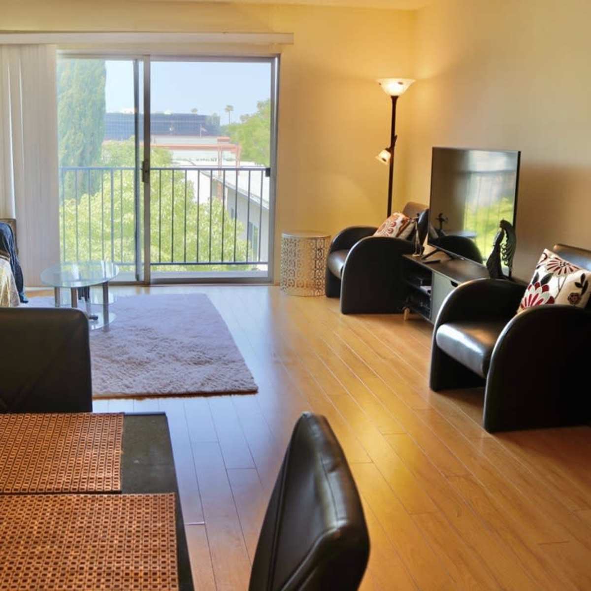 A modern living room with a large window, a couch and chairs, a glass coffee table, and a television.