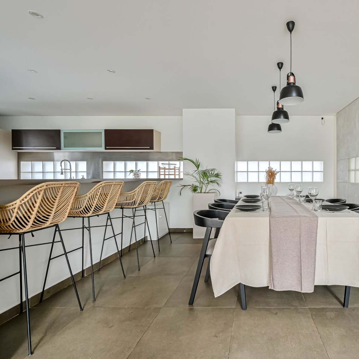 A modern dining area features a table set for a meal, with black chairs and pendant lighting overhead.