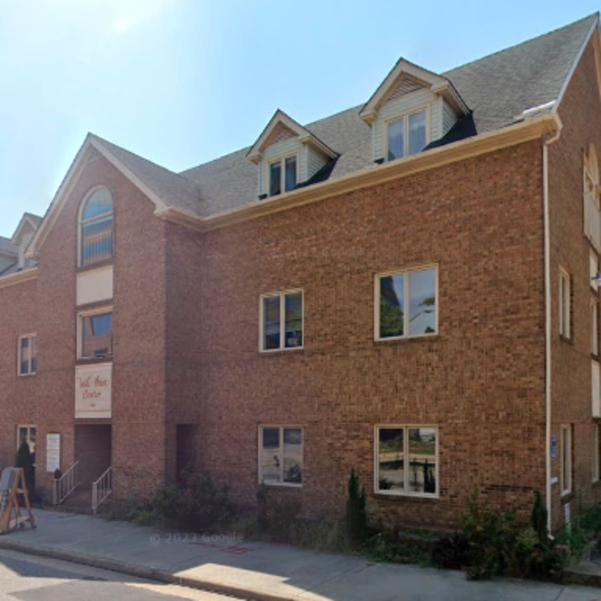 A three-story brick building with multiple windows, located on a corner near a glass-fronted office building.