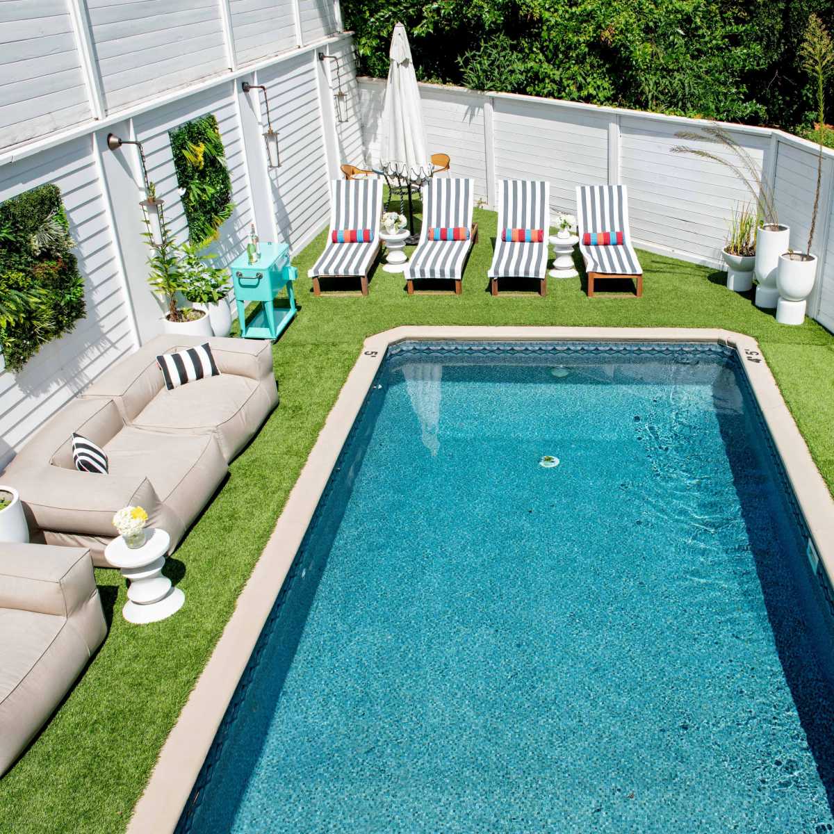 A backyard swimming pool surrounded by two sets of lounge chairs and outdoor seating on a grass-like surface.