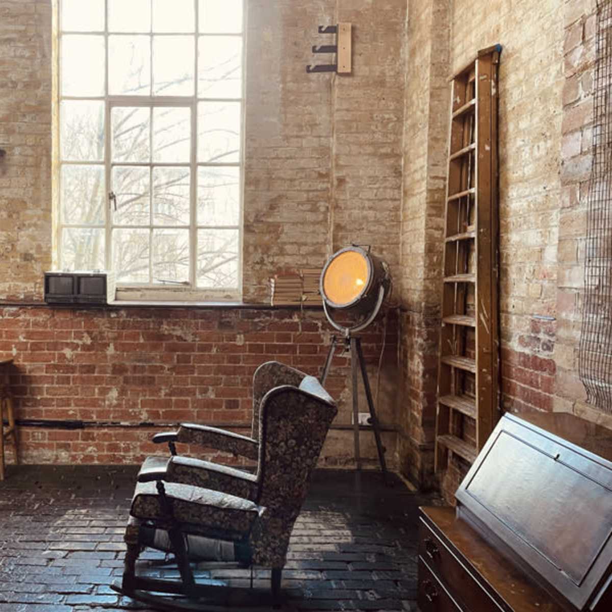 A rustic interior space with exposed brick walls, a vintage rocking chair, a spotlight, and wooden furniture.