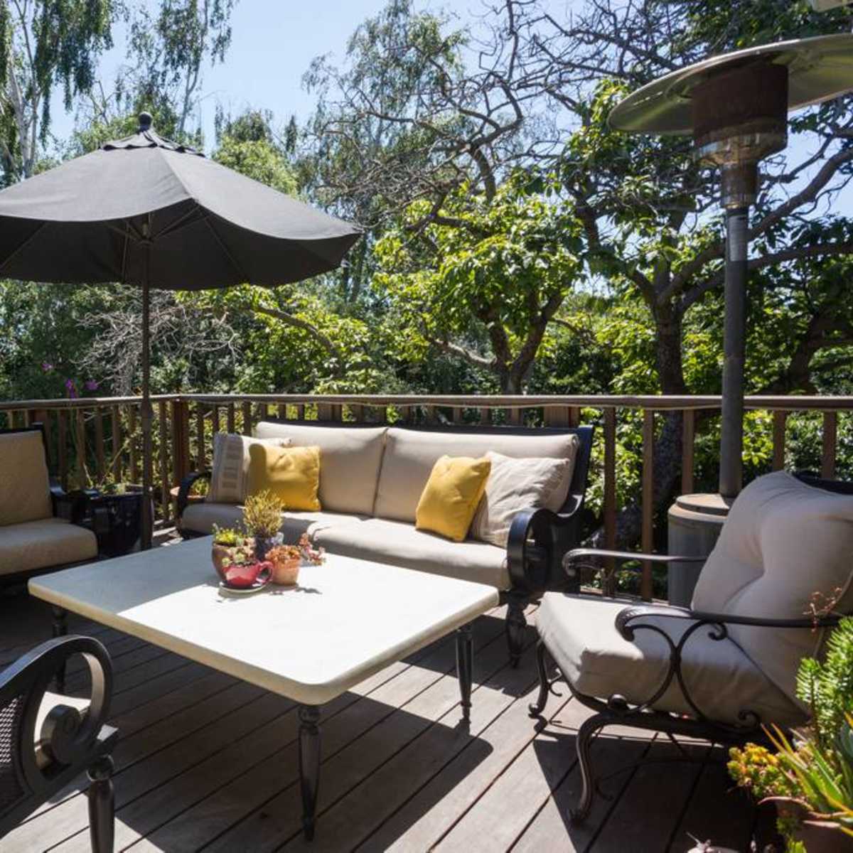A patio area features a table and several chairs beneath a large umbrella, surrounded by greenery.
