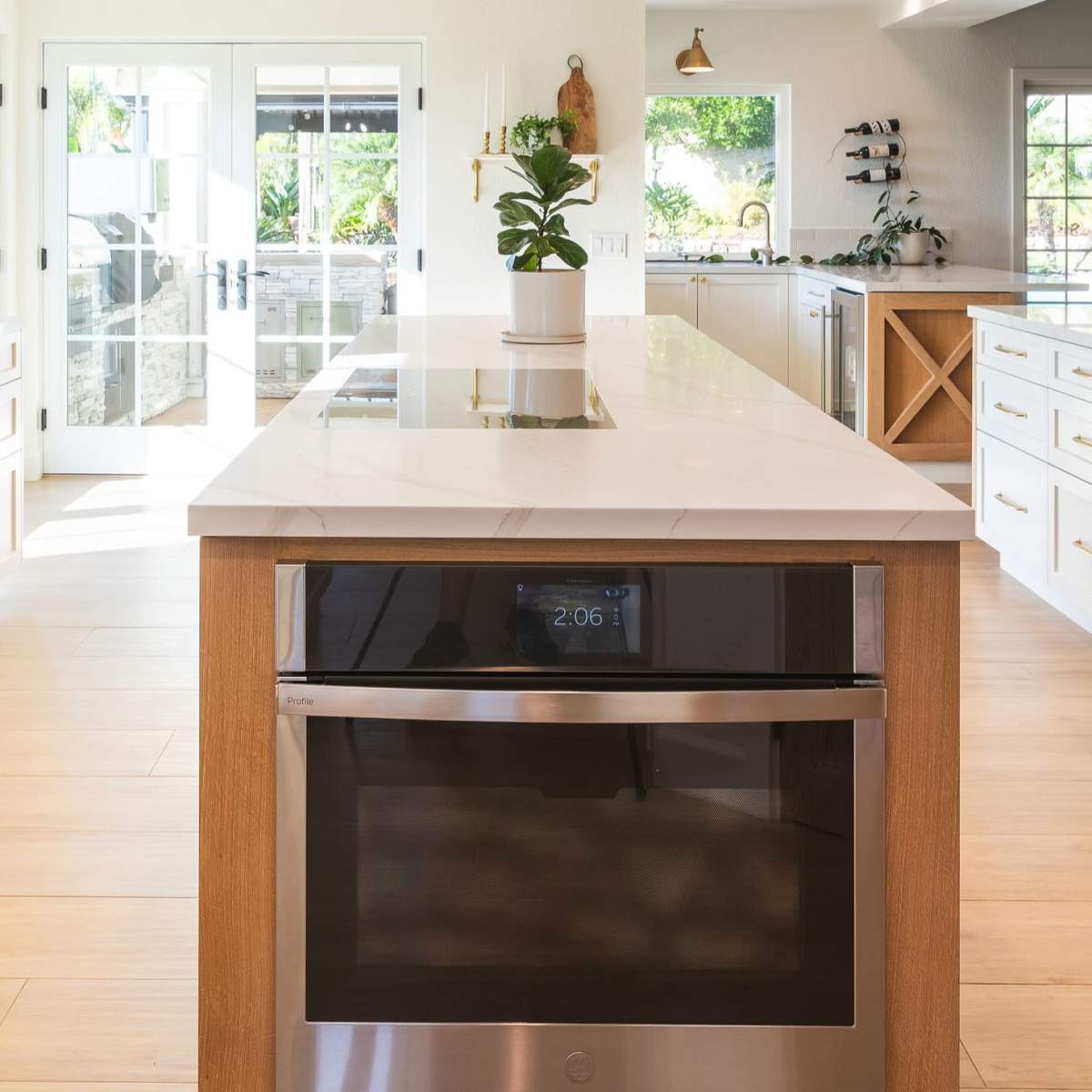 A modern kitchen with a large island, equipped with a cooktop, stainless steel oven below, and bright natural light coming through the windows.