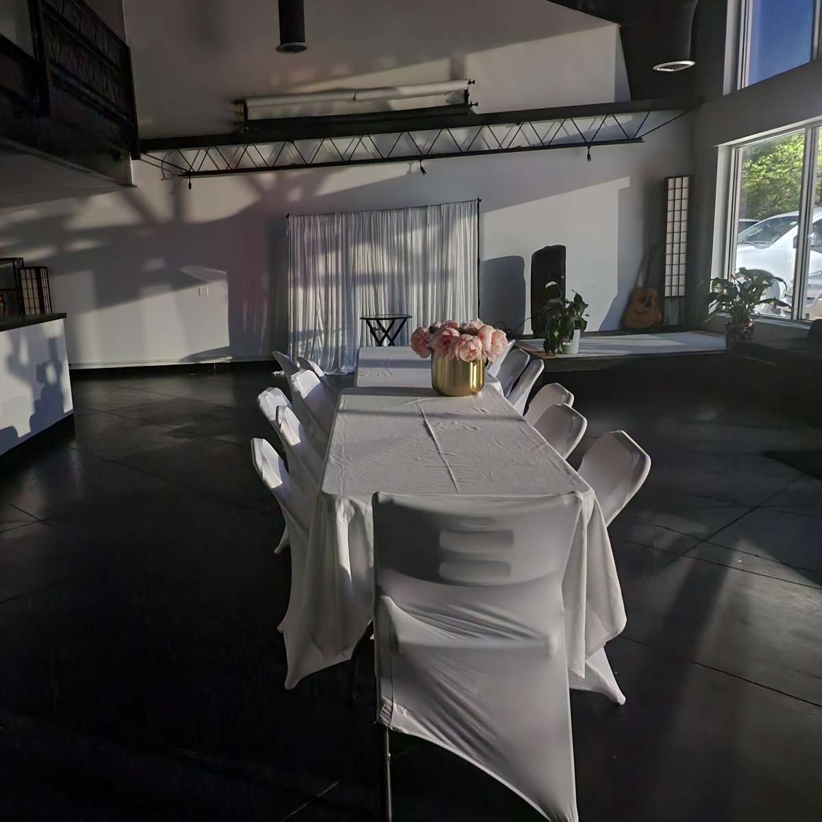 A long table with a white tablecloth is set in a modern, well-lit room featuring a mix of seating and greenery.