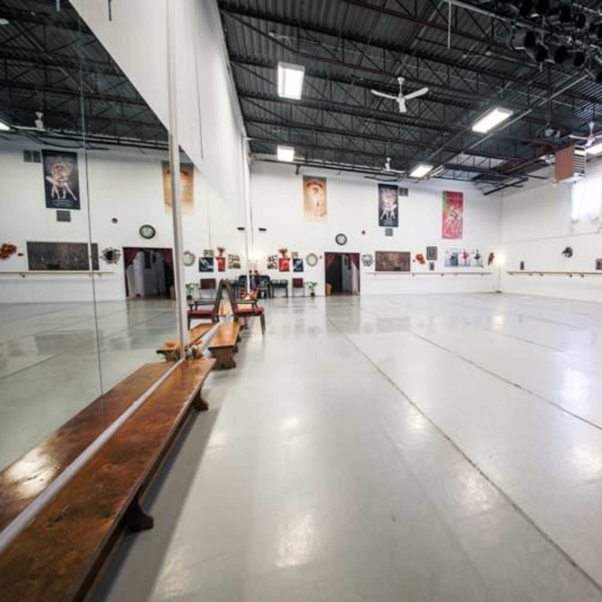 A spacious dance studio with mirrors, a wooden ballet bar, and framed photographs on the walls.