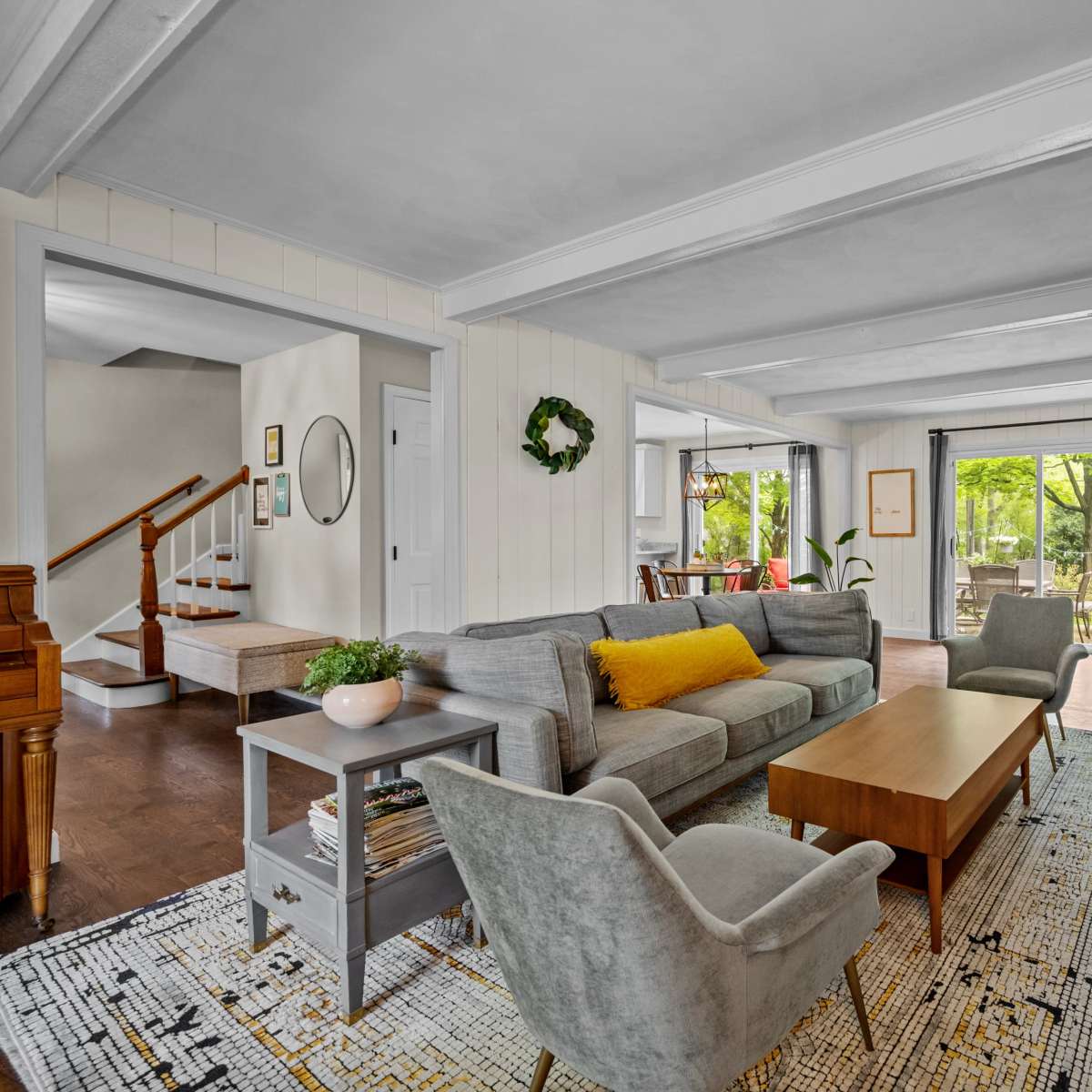 A spacious living room featuring a gray sofa, light-colored chairs, a wooden coffee table, and a fireplace, with large windows that open to a garden view.