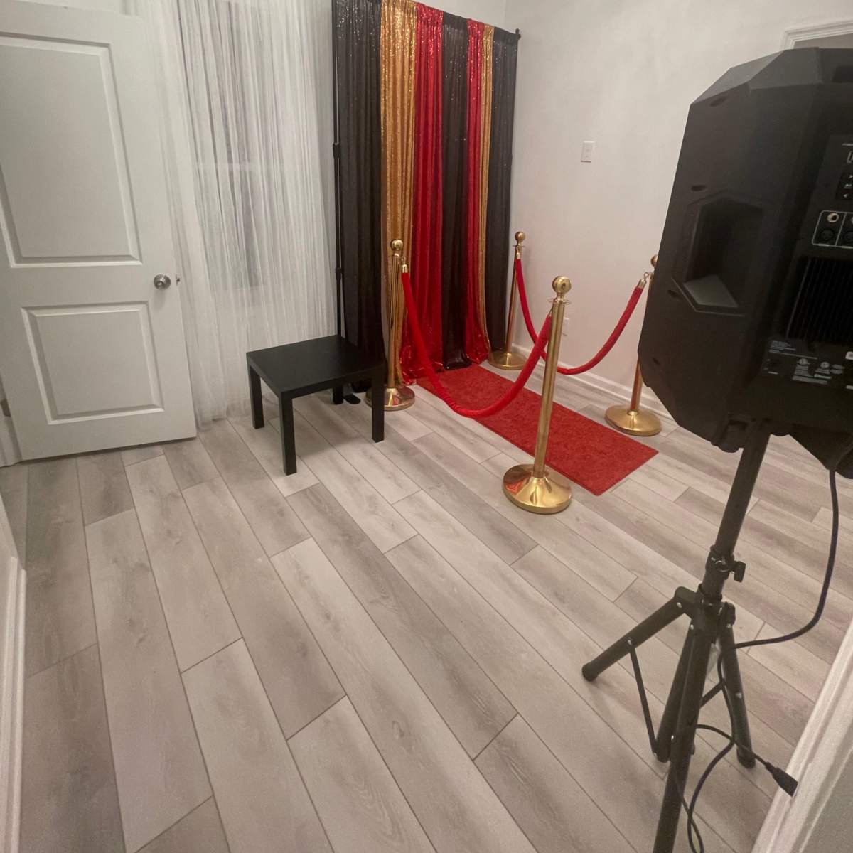 A small room with a red carpet, a decorative backdrop of curtains in gold, black, and red, and a speaker next to a black table.
