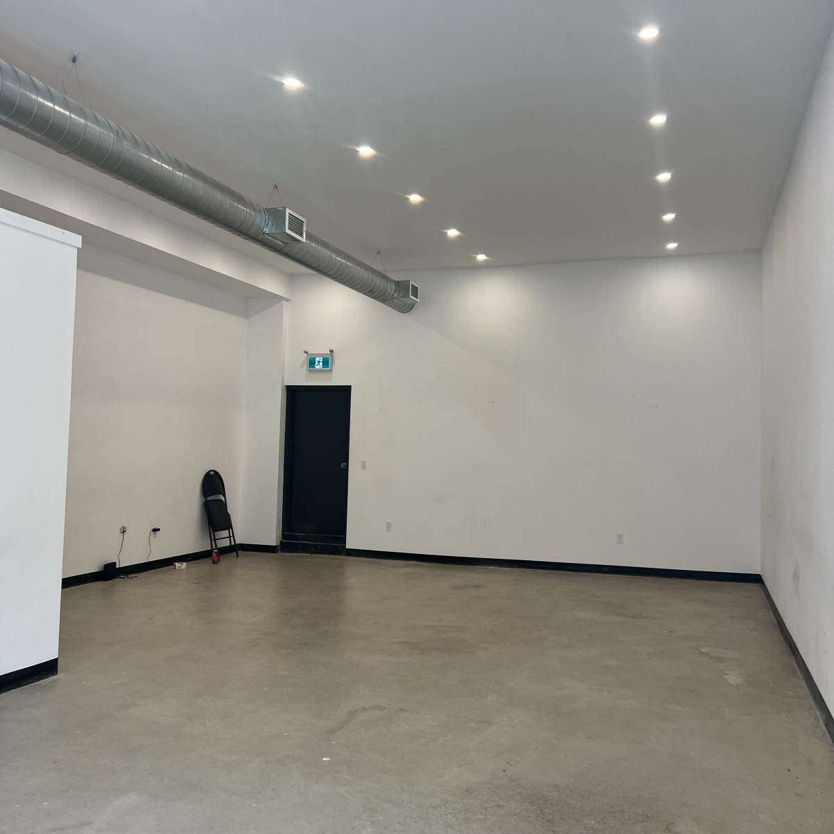 A large, empty room with smooth concrete floors, white walls, and a black door at one end.