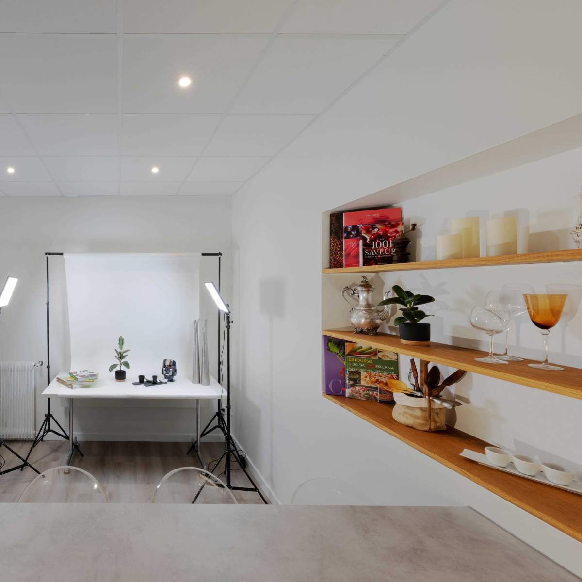 A well-lit studio space with a table, photography equipment, and styled shelves displaying decorative items.