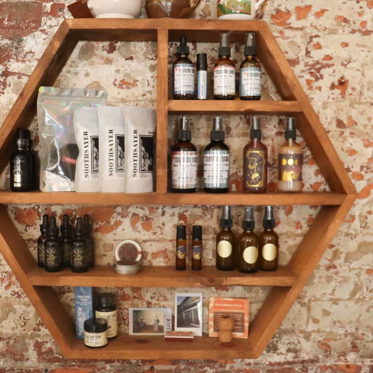 A honeycomb-shaped wooden shelf displays various bottles and packages of skincare products against a rustic brick wall.