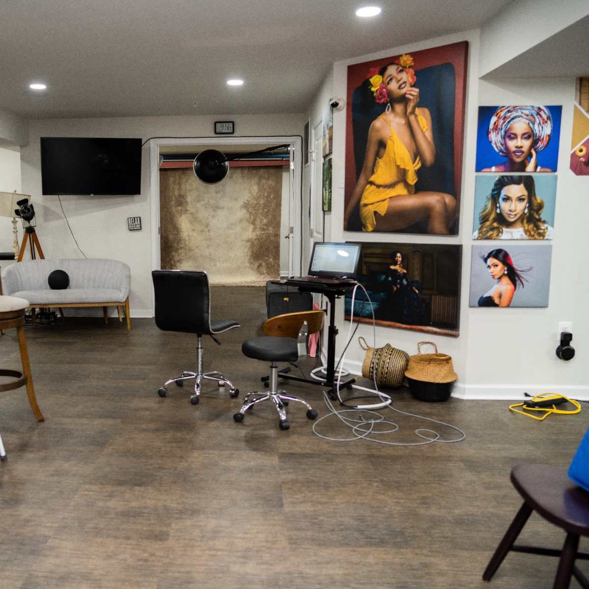 A spacious studio with various chairs, a couch, and multiple framed portraits hanging on the walls.