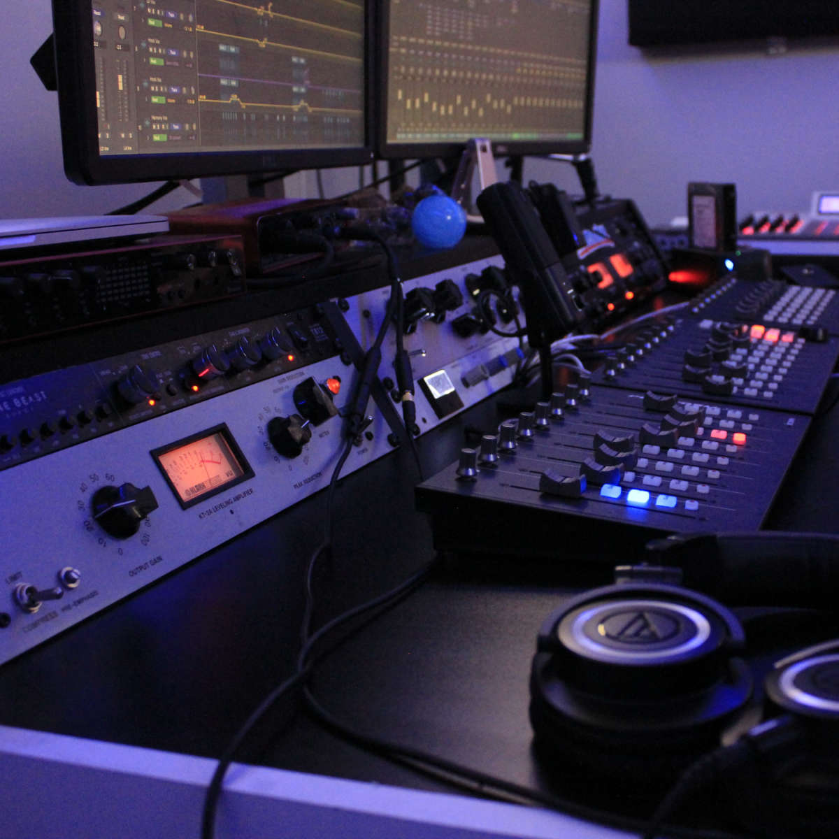 A music production studio with multiple monitors, audio equipment, and a set of headphones on a desk.